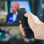 A man with a remote control in his hand switches channels on the TV