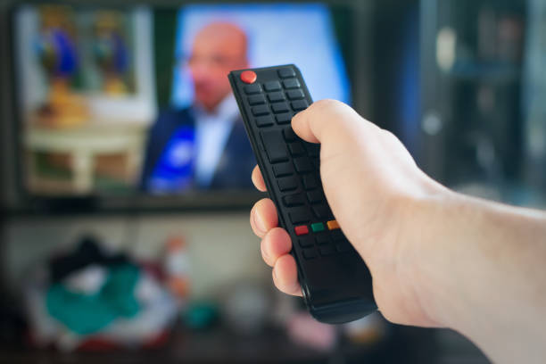 A man with a remote control in his hand switches channels on the TV