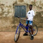 Joshua Anum, who had his left arm amputated 7 years ago, sits on a bicycle at his home, in Abuja