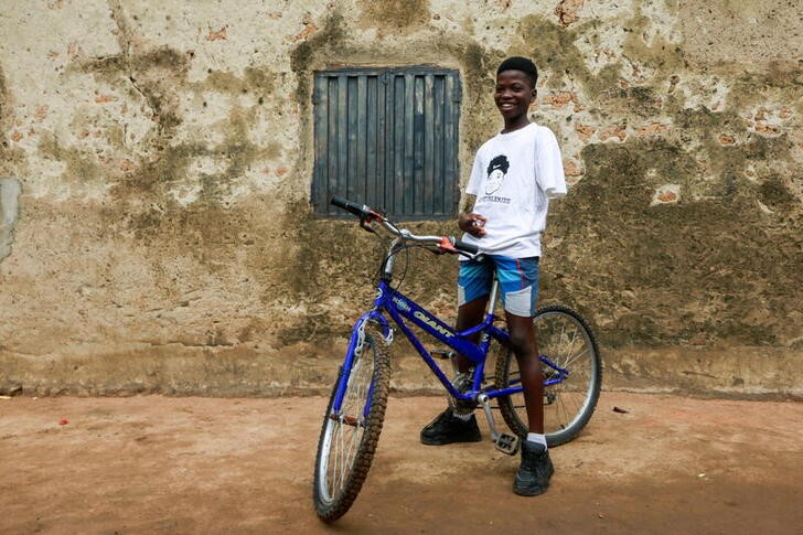 Joshua Anum, who had his left arm amputated 7 years ago, sits on a bicycle at his home, in Abuja